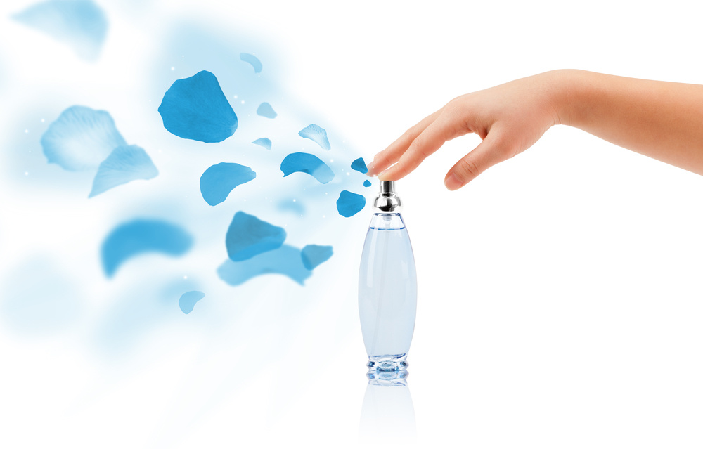 close up of woman hands spraying rose petals from beautiful perfume bottle